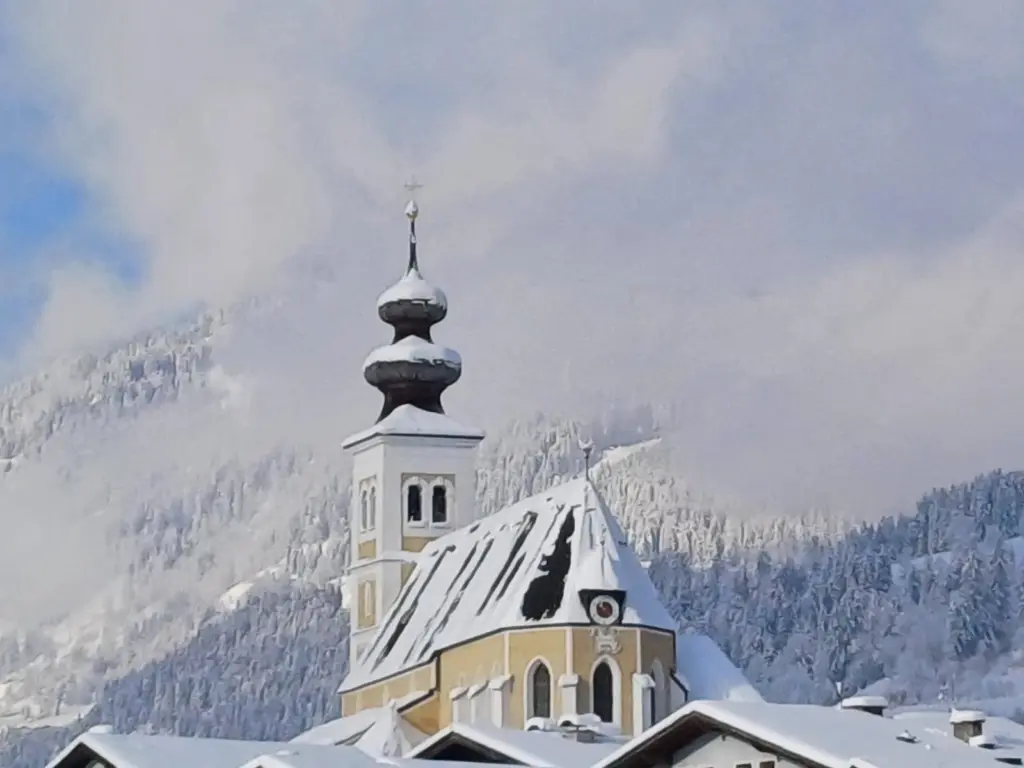 Pfarrkirche St. Veit mit verschneitem Dach vor dem Winterwald