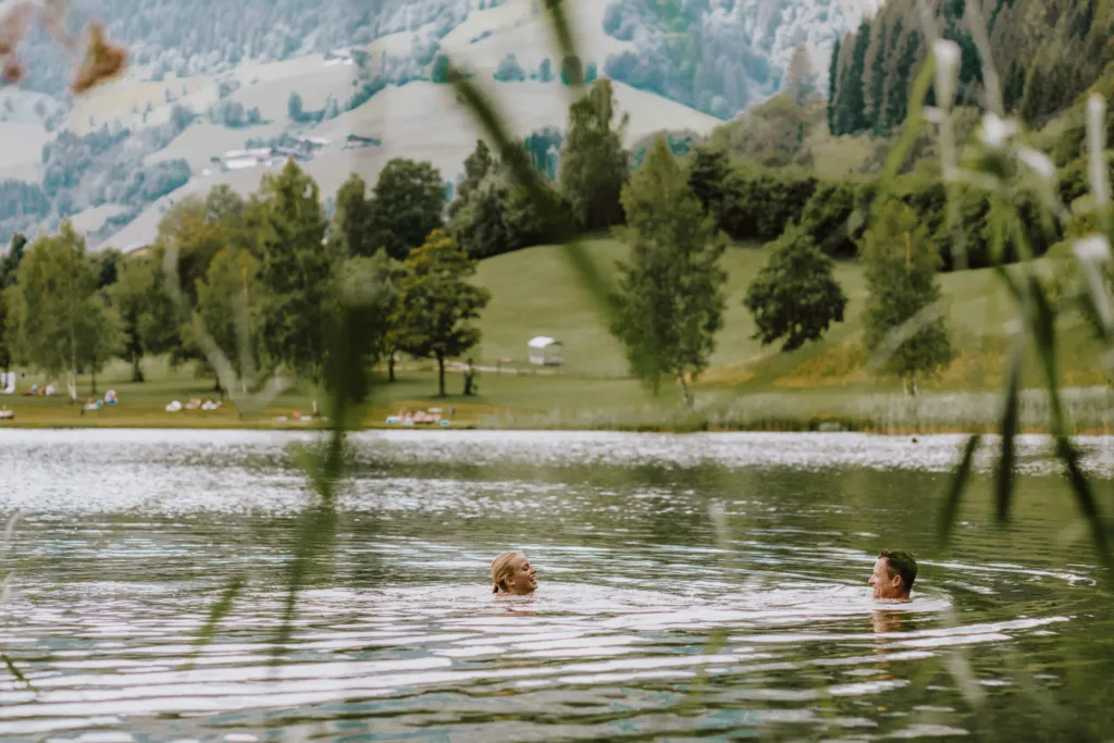Schwimmen in einem Badesee auf der Sonnenterrasse, im Hintergrund Wiesen und Bäume