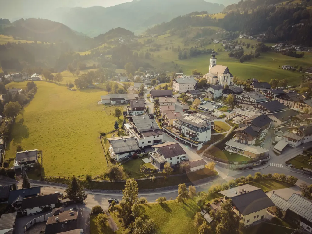 Pfarrkirche St. Veit über dem Ort, umgeben von Wiesen und Bergen im Sonnenlicht