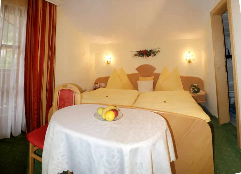 Doppelzimmer mit hellem Holzbett, Wandleuchten und kleinem Tisch